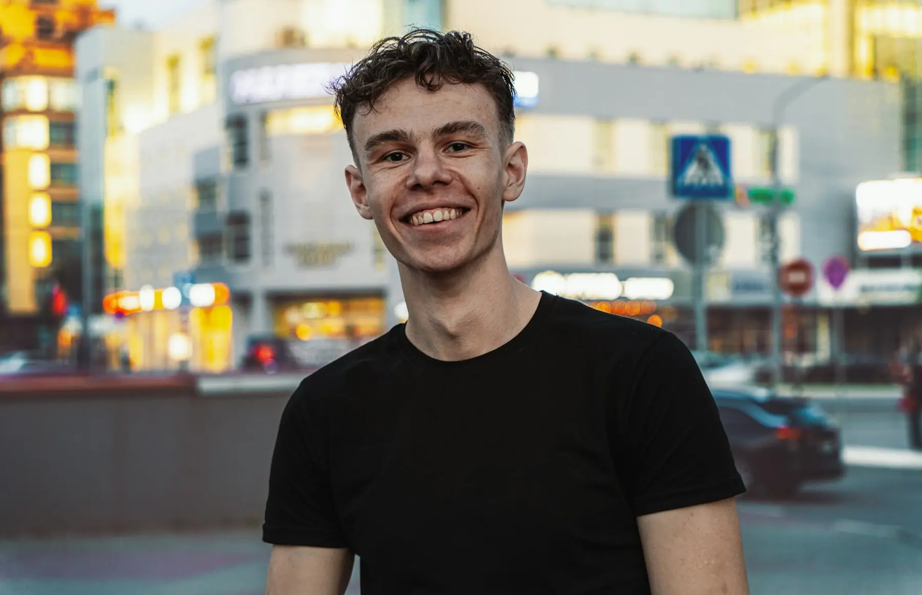 Smiling man in a black t-shirt on a city street at dusk